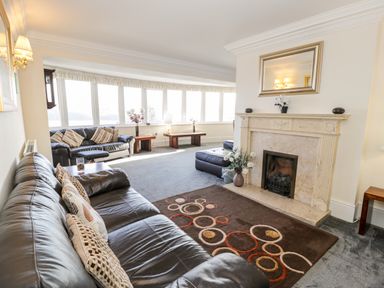 A living room with leather sofas a fireplace a rug with circular patterns and large windows at 11 Glyn Garth Mews in Llandegfan near Beaumaris