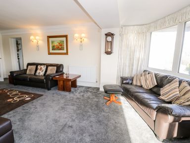 A living room with two leather sofas a wooden coffee table a wall clock and large windows at 11 Glyn Garth Mews Llandegfan near Beaumaris