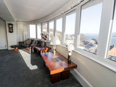 A living room with large windows a leather sofa wooden tables and flowers at 11 Glyn Garth Mews in Llandegfan near Beaumaris