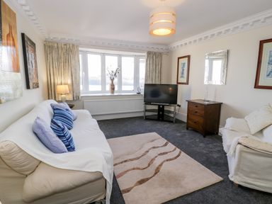A living room with two sofas a television on a stand a wooden chest of drawers and a beige rug at 11 Glyn Garth Mews in Llandegfan near Beaumaris
