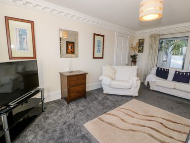 A living room with white sofas a carpet a wooden side table a television and framed pictures on walls at 11 Glyn Garth Mews in Llandegfan near Beaumaris