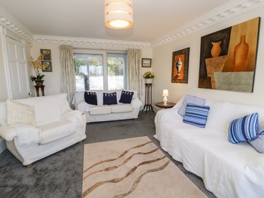 A living room with three white sofas a beige carpet and wall art at 11 Glyn Garth Mews Llandegfan near Beaumaris