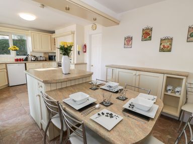 A kitchen with a countertop dining area set with plates utensils and glasses and a vase with flowers on the island at 11 Glyn Garth Mews Llandegfan near Beaumaris