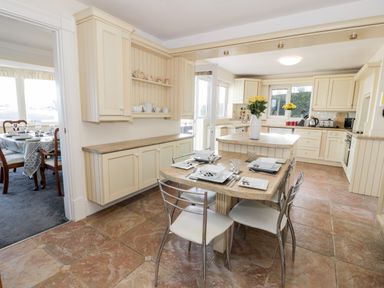 A kitchen with an island table set for four with plates and cutlery and a dining room with a table and chairs visible through a doorway at 11 Glyn Garth Mews in Llandegfan near Beaumaris