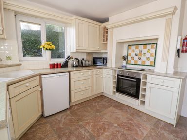A kitchen with beige cabinets a white dishwasher oven microwave and utensils on counter at 11 Glyn Garth Mews Llandegfan near Beaumaris
