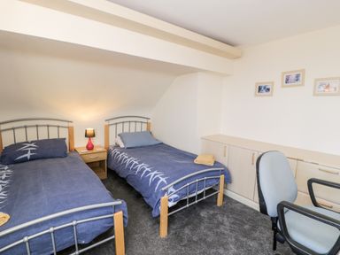 A bedroom with two single beds a bedside table with a lamp an office chair and storage cabinets at 11 Glyn Garth Mews in Llandegfan near Beaumaris