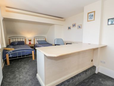 A bedroom with two single beds a desk with a chair and framed pictures on the walls at 11 Glyn Garth Mews in Llandegfan near Beaumaris
