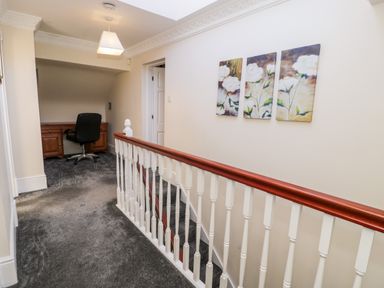 A hallway with grey carpet and a wooden desk with a black office chair at 11 Glyn Garth Mews in Llandegfan near Beaumaris
