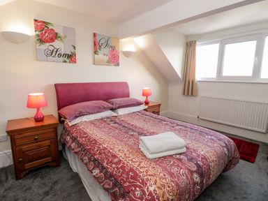 A bedroom with a double bed two bedside tables with lamps wall art and a window at 11 Glyn Garth Mews Llandegfan near Beaumaris