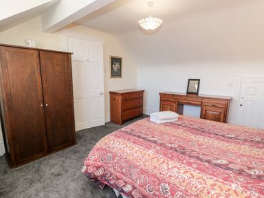 A bedroom with a bed with patterned bedspread two wooden dressers a wardrobe and a door at 11 Glyn Garth Mews in Llandegfan near Beaumaris