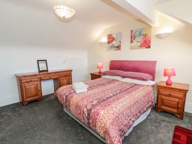A bedroom with a bed with patterned bedding two bedside tables with lamps a wooden desk and artwork on the wall at 11 Glyn Garth Mews in Llandegfan near Beaumaris