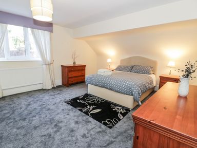 A bedroom with a bed two side tables two dressers a window with curtains and a carpet at 11 Glyn Garth Mews in Llandegfan near Beaumaris
