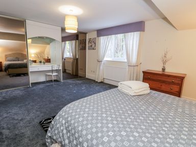 A bedroom with a bed folded towels on it a wooden chest of drawers a window with curtains a dressing table with chair and mirrored wardrobes at 11 Glyn Garth Mews in Llandegfan near Beaumaris