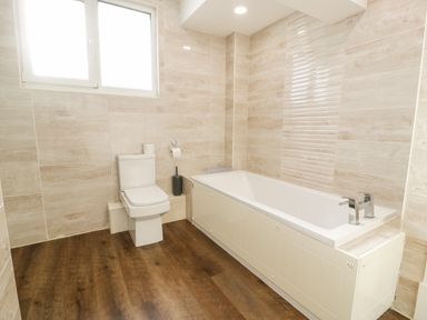 A bathroom with a toilet and a bathtub with faucet at 11 Glyn Garth Mews in Llandegfan near Beaumaris