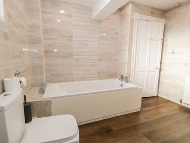 A bathroom with a bathtub toilet and door at 11 Glyn Garth Mews Llandegfan near Beaumaris