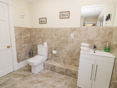 A bathroom with a toilet and a white cabinet sink with towels and soap at 11 Glyn Garth Mews in Llandegfan near Beaumaris