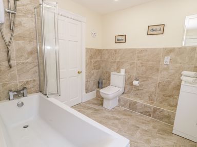 A bathroom with a bathtub toilet and a cabinet with towels at 11 Glyn Garth Mews in Llandegfan near Beaumaris