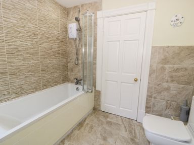 A bathroom with a bathtub shower combination a white door and a toilet at 11 Glyn Garth Mews in Llandegfan near Beaumaris