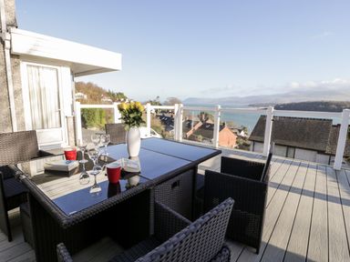 An outdoor patio with a dining table and chairs overlooking rooftops and water at 11 Glyn Garth Mews in Llandegfan near Beaumaris