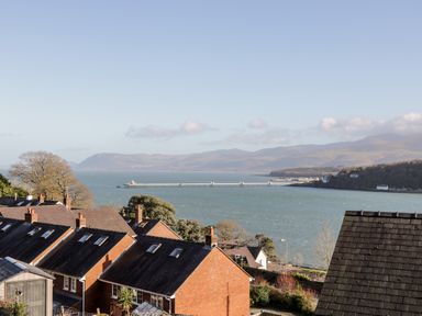 A coastal view with brick houses in the foreground a pier over the water and hills in the background at 11 Glyn Garth Mews in Llandegfan near Beaumaris