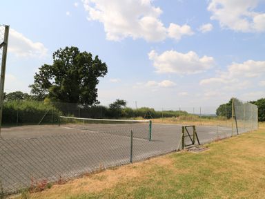 A tennis court with a net and fence at The Apple Shed, Motcombe