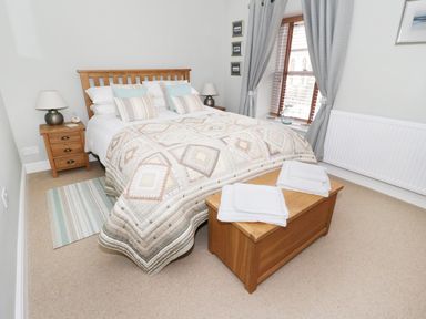 A bedroom with a wooden bed frame bedside tables lamps and folded towels on a chest at Llwyn Onn in Dolwyddelan