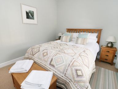 A bedroom with a wooden bed, patterned quilt, bedside tables with lamps, and folded towels on a wooden chest at Llwyn Onn in Dolwyddelan