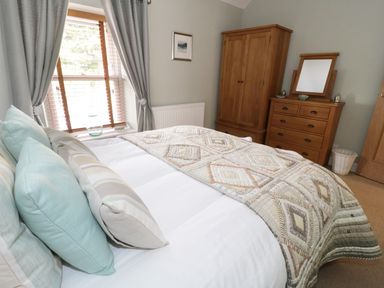 A bedroom with a bed with cushions and a quilt a window with curtains a wooden wardrobe and a wooden dresser with a mirror at Llwyn Onn in Dolwyddelan