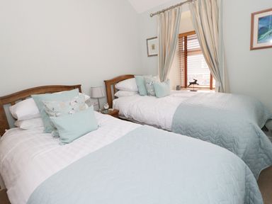 A bedroom with two single beds side by side with wooden headboards light blue bedding a bedside table with a lamp and clock and a window with curtains at Llwyn Onn in Dolwyddelan