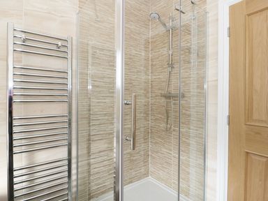 A shower enclosure with glass doors a chrome towel radiator and a wooden door in a bathroom at Llwyn Onn in Dolwyddelan