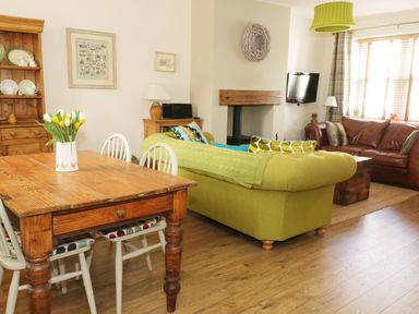 A living room with a wooden dining table and chairs a green sofa a brown leather sofa a wall-mounted TV and a fireplace at Llwyn Onn in Dolwyddelan