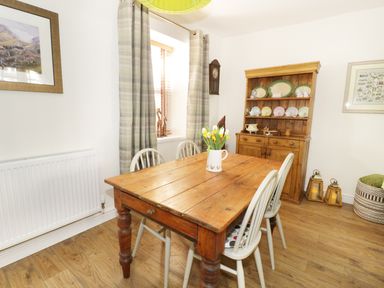 A dining room with a wooden table and four chairs a vase with flowers on the table and a wooden cabinet with plates at Llwyn Onn in Dolwyddelan
