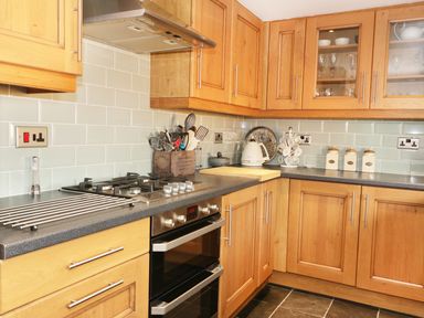 A kitchen with wooden cabinets a gas stove utensils kettle and countertop containers at Llwyn Onn in Dolwyddelan