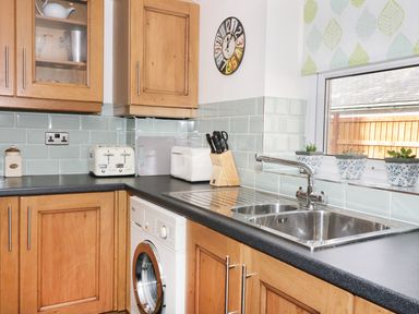 A kitchen with wooden cabinets a washing machine a stainless steel sink and potted plants on the windowsill at Llwyn Onn in Dolwyddelan