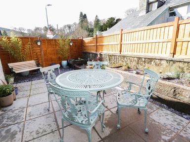 An outdoor patio with a round metal table and four chairs a wooden bench plants and fenced walls at Llwyn Onn in Dolwyddelan