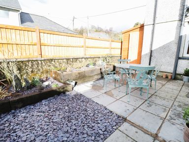 An outdoor patio area with metal table and chairs a wooden shed gravel and raised garden beds at Llwyn Onn in Dolwyddelan