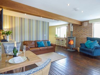 A living room with a brown leather sofa a blue armchair a wood burning stove and a dining table with champagne at Blue Oyster in Mullion near Lizard Point