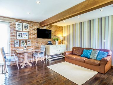 A living room with a leather sofa next to a striped wall and a small dining table with two chairs near a brick wall at Blue Oyster in Mullion near Lizard Point