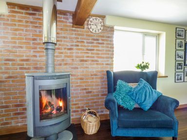 A room with a wood burning stove on a brick wall and a blue armchair with cushions at Blue Oyster in Mullion near Lizard Point