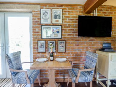 A small dining area with a wooden table set for two chairs and framed pictures on a brick wall at Blue Oyster in Mullion near Lizard Point