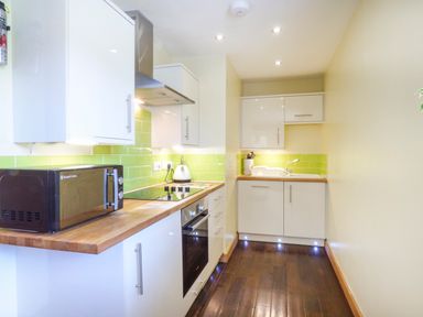 A kitchen with white cabinets green tiled backsplash wooden countertops a microwave and a stove at Blue Oyster in Mullion near Lizard Point