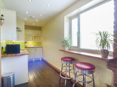 A narrow kitchen with a countertop microwave two bar stools under a window and potted plants at Blue Oyster in Mullion near Lizard Point