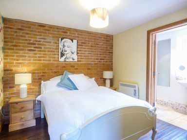 A bedroom with a double bed between two bedside tables with lamps and an en suite bathroom at Blue Oyster in Mullion near Lizard Point