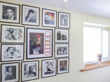 A wall with framed black and white photographs and a framed poster near a window with a glass vase of colorful balls at Blue Oyster in Mullion near Lizard Point