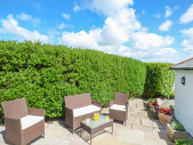 A patio with wicker chairs and a table with drinks surrounded by green hedges at Blue Oyster in Mullion near Lizard Point