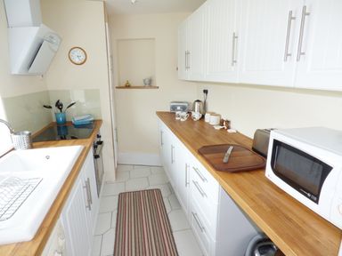A kitchen with white cabinets wooden countertops a microwave a kettle a toaster and a striped rug at The Packing House in Hanley Castle near Malvern