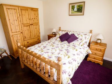 A bedroom with a wooden bed with floral bedding two purple pillows wooden bedside tables with lamps wooden wardrobe and a purple rug at The Packing House in Hanley Castle near Malvern