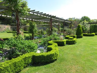 A garden with trimmed hedges climbing plants on wooden pergolas and grass at The Packing House in Hanley Castle near Malvern