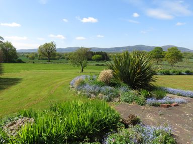 A garden with grass and flowering plants with trees and hills in the background at The Packing House in Hanley Castle near Malvern