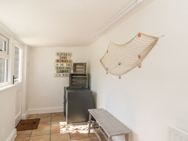 A small room with a wooden bench a black cabinet with wooden crates on top a fishing net on the wall and a door with an anchor doormat at Marsh Villa in Silloth